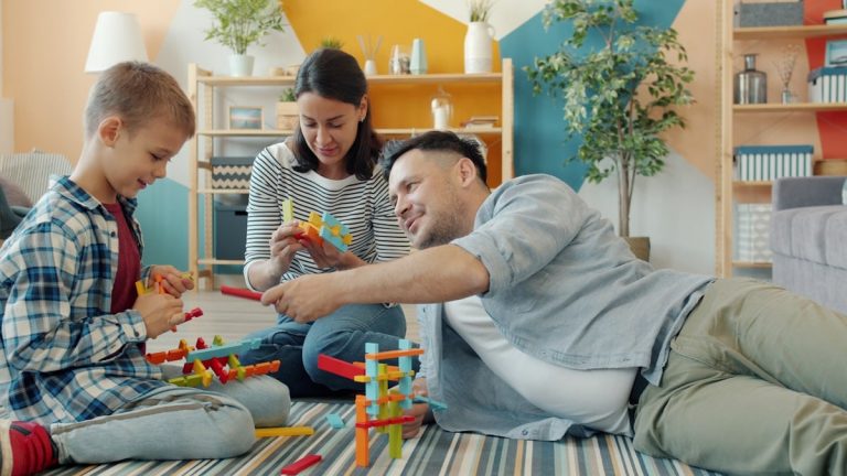 Child is playing with mother and father cheerful adults at home building with construction blocks sitting on floor together. Youth and family concept.