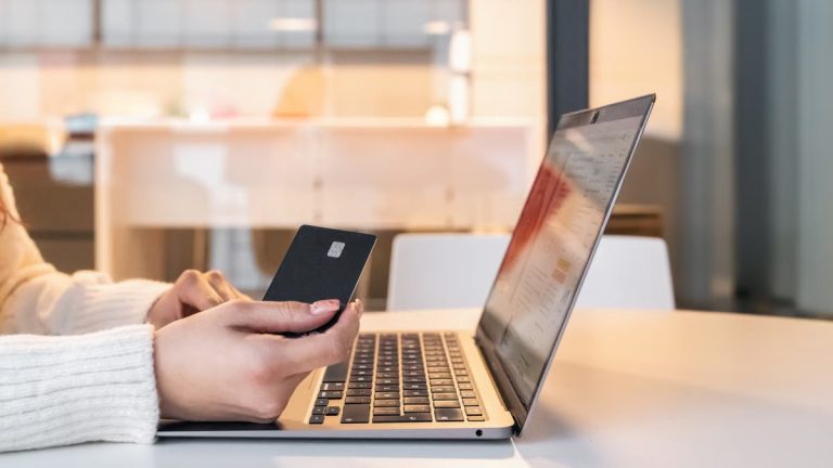 A woman using a credit card and laptop for online shopping in a modern indoor setting.